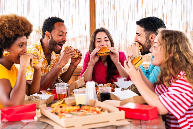 Foto grupo multiétnico de jovens amigos felizes jantando churrasco no telhado em casa