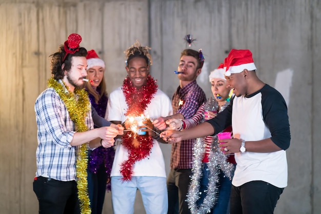 grupo multiétnico de jovens empresários casuais felizes acendendo um diamante e se divertindo enquanto comemora a véspera de ano novo em frente a parede de concreto no novo escritório de inicialização