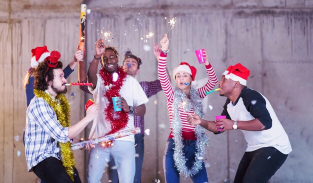 grupo multiétnico de jovens empresários casuais felizes dançando e fazendo festa de confete enquanto comemora a véspera de ano novo em frente a parede de concreto no novo escritório de inicialização