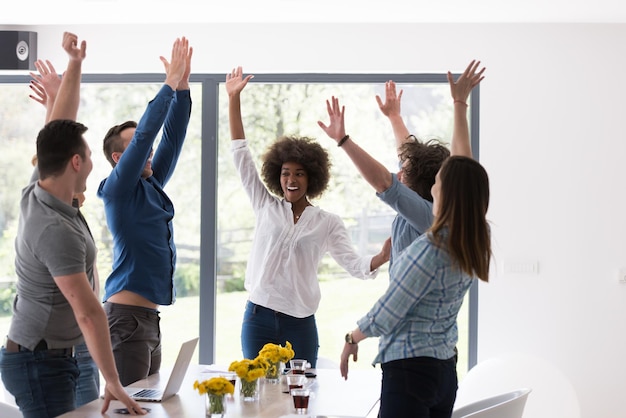 Foto grupo multiétnico de jovens empresários que parecem felizes enquanto comemoram o sucesso em seus locais de trabalho no escritório de inicialização