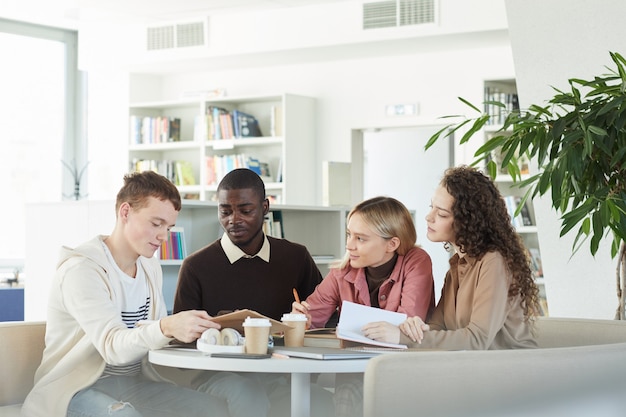 Grupo multiétnico de jovens estudando juntos enquanto estão sentados à mesa na biblioteca da faculdade e trabalhando em um projeto em grupo,