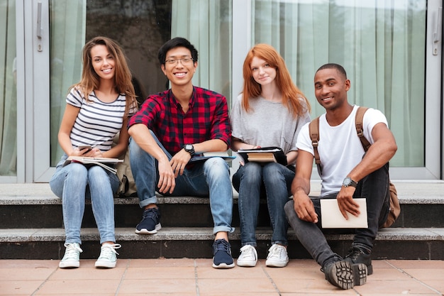 Grupo multiétnico de jovens felizes sentados juntos no campus