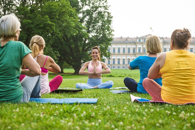 Grupo multiétnico de mulheres idosas treinando no parque com instrutor de fitness - Idosos ativos praticando esportes na natureza