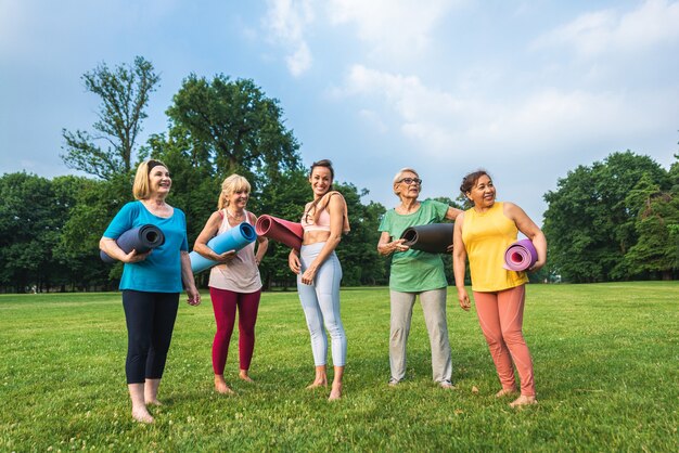 Grupo multiétnico de mulheres idosas treinando no parque com instrutor de fitness - Idosos ativos praticando esportes na natureza