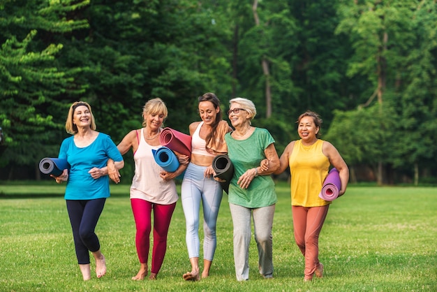 Grupo multiétnico de mulheres idosas treinando no parque com instrutor de fitness - Idosos ativos praticando esportes na natureza