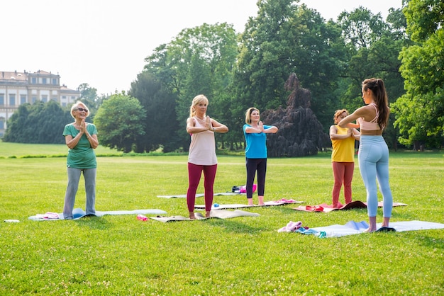 Grupo multiétnico de mulheres idosas treinando no parque com instrutor de fitness - Idosos ativos praticando esportes na natureza