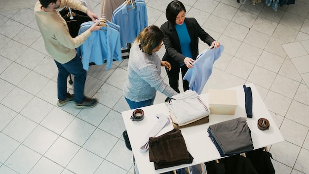 Grupo multiétnico de pessoas comprando roupas na loja de varejo, verificando novas mercadorias no shopping. Homens e mulheres comprando roupas formais ou casuais, tentando aumentar o guarda-roupa.