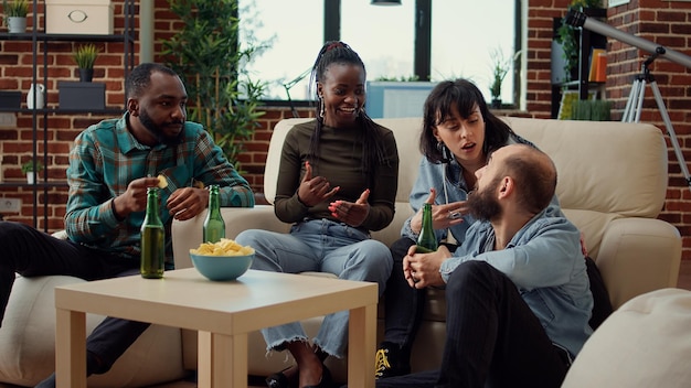 Grupo multiétnico de pessoas falando sobre amizade e bebendo cerveja de garrafas para se divertir em casa reunindo. Amigos rindo e curtindo a atividade de fim de semana juntos, relaxando.