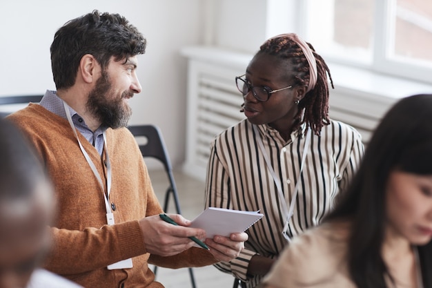 Grupo multiétnico de pessoas na audiência da conferência de negócios com foco no homem barbudo falando com uma mulher afro-americana enquanto está sentado em cadeiras