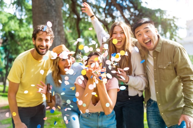 Grupo multiétnico de retrato de festa jogando confete sorrindo na diversão do parque com o conceito de amigos