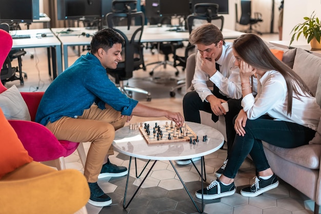 Grupo multiétnico de empresarios jugando al ajedrez mientras descansan en el área de relajación en la moderna oficina de inicio. foto de alta calidad