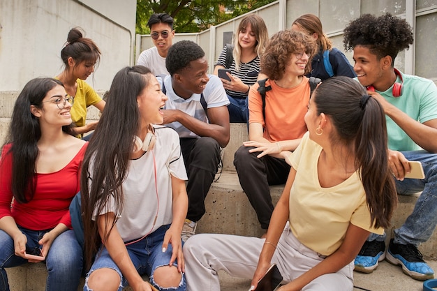 Grupo multiétnico de estudiantes felices en un descanso los jóvenes se ríen sentados en las escaleras del alto ...