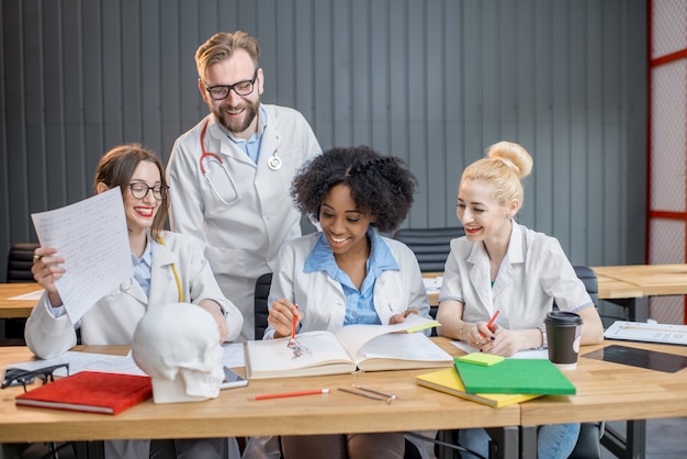 Foto grupo multiétnico de estudiantes de medicina en uniforme estudiando juntos sentados en el escritorio con libros en el aula moderna