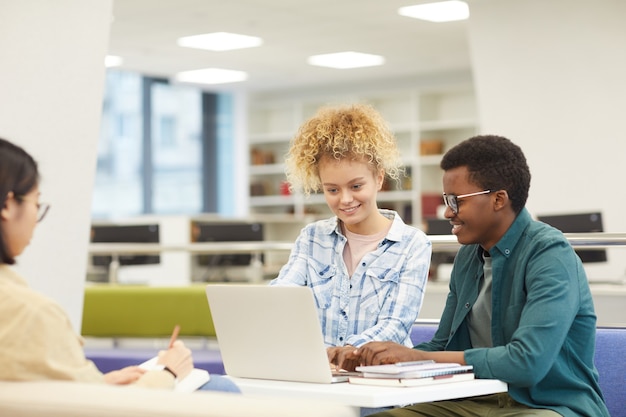 Grupo multiétnico de estudiantes usando laptop y sonriendo felizmente