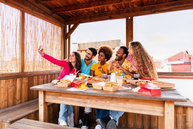 Foto grupo multiétnico de jóvenes amigos felices cenando barbacoa en la azotea en casa