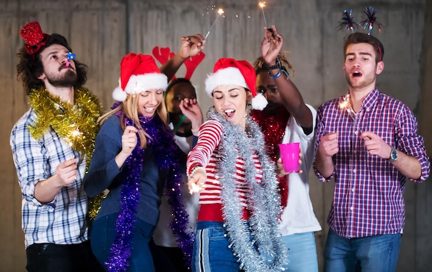 grupo multiétnico de jóvenes empresarios casuales felices bailando con bengalas y divirtiéndose mientras celebran la víspera de año nuevo frente a un muro de hormigón en la nueva oficina de inicio