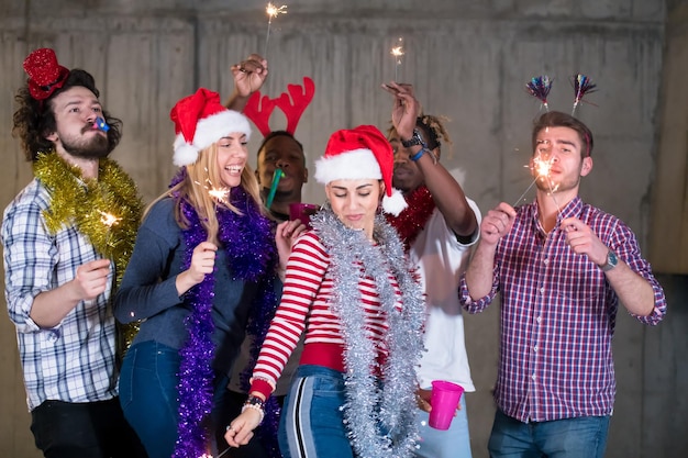 grupo multiétnico de jóvenes empresarios casuales felices bailando con bengalas y divirtiéndose mientras celebran la víspera de año nuevo frente a un muro de hormigón en la nueva oficina de inicio