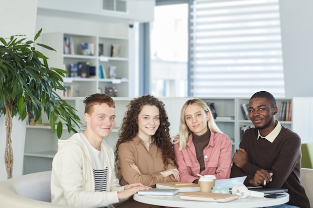 Grupo multiétnico de jóvenes sonrientes mientras estudian juntos sentados a la mesa en la biblioteca de la universidad,