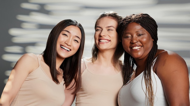 Grupo multiétnico de modelos posando para un anuncio de positividad corporal en el estudio, divirtiéndose con amigos anunciando productos para el cuidado de la piel. Mujeres alegres riendo en cámara, diferentes tonos de piel y tipos de cuerpo.