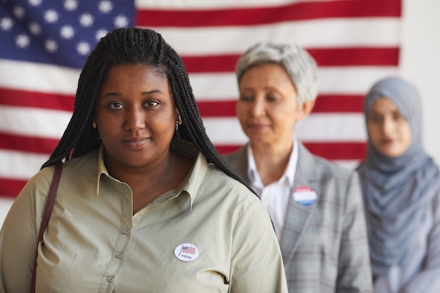 Grupo multiétnico de personas en la mesa de votación el día de las elecciones, se centran en la mujer afroamericana sonriente con la etiqueta VOTÉ, espacio de copia