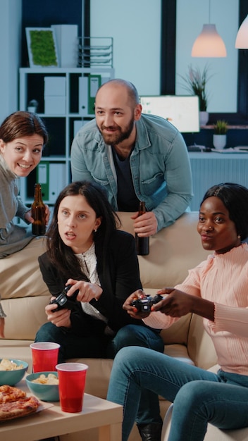 Grupo multiétnico de personas que usan joysticks para jugar videojuegos en la consola de televisión para entretenerse después del trabajo. Compañeros de trabajo jugando con controladores en la televisión para hacer una actividad divertida.