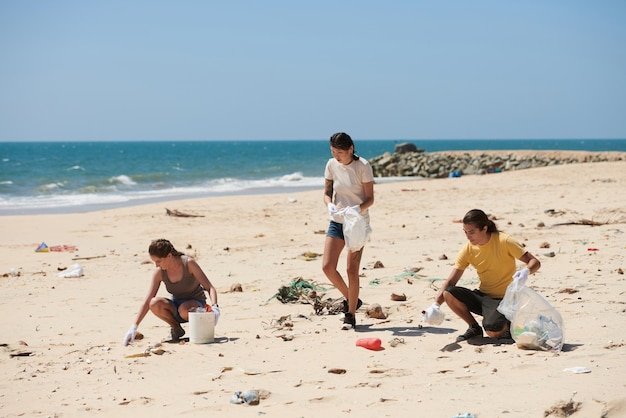 Grupo multiétnico de voluntarios con bolsas de basura limpiando la playa en un día soleado