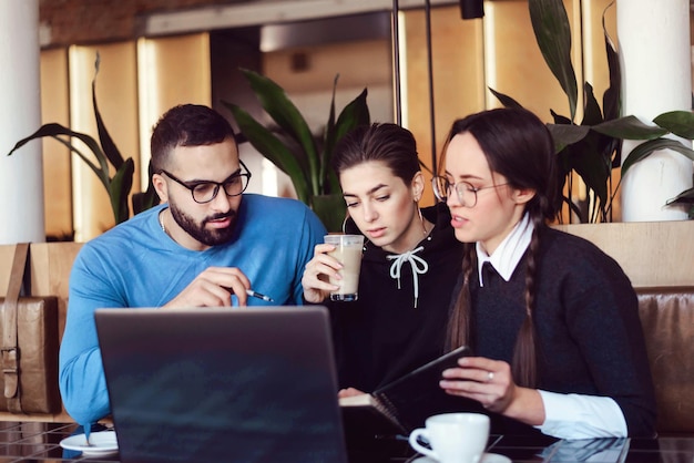 Grupo multinacional de estudiantes alegres que estudian en el café.