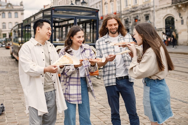 Grupo multirracial de amigos comiendo una pizza en una calle del casco antiguo
