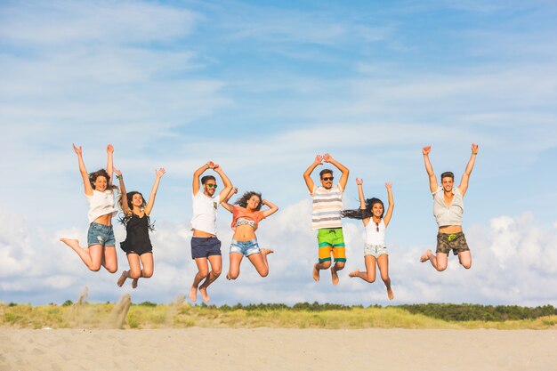 Grupo multirracial de amigos saltando en la playa.