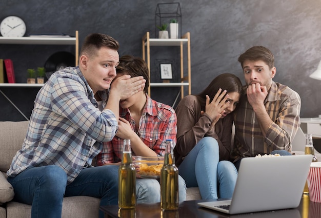 Grupo multirracial de amigos assustados assistindo filme no laptop e comendo pipoca