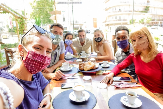 Grupo multirracial de amigos usando máscara de proteção no restaurante