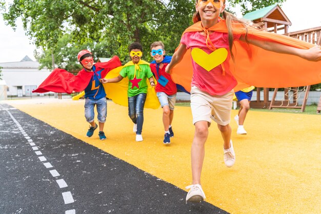 Grupo multirracial de jovens escolares vestindo fantasias de super-heróis e se divertindo ao ar livre