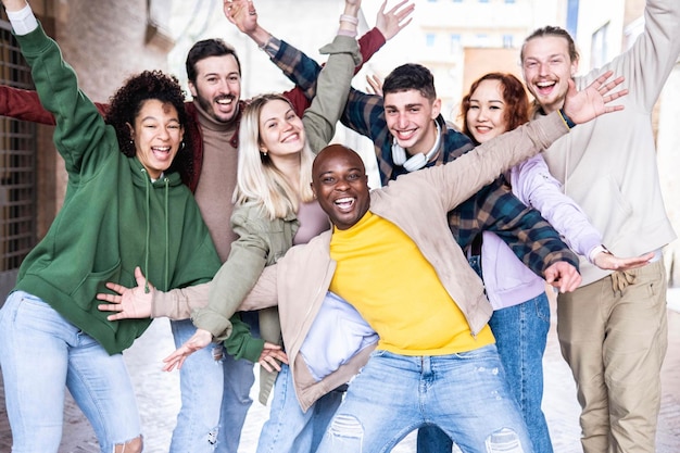 Grupo multirracial de pessoas com as mãos para cima sorrindo para a câmera do lado de fora