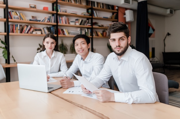 Grupo multirracial de jóvenes empresarios en una oficina moderna trabajando con laptop y papeles