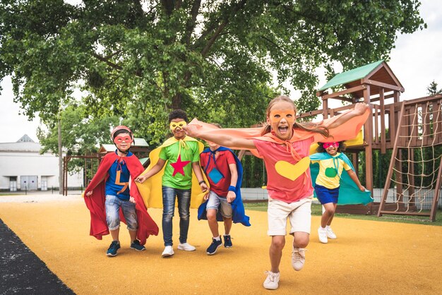 Grupo multirracial de jóvenes escolares vistiendo trajes de superhéroe y divirtiéndose al aire libre