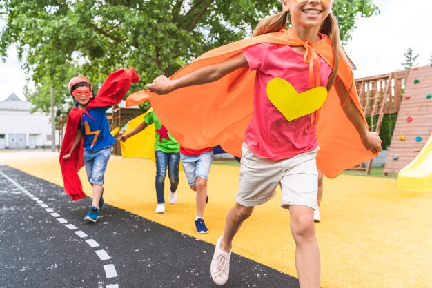 Grupo multirracial de jóvenes escolares vistiendo trajes de superhéroe y divirtiéndose al aire libre