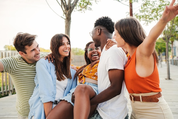 Grupo multirracial de jóvenes felices que llevan a su compañero de clase universitario para celebrar sus calificaciones