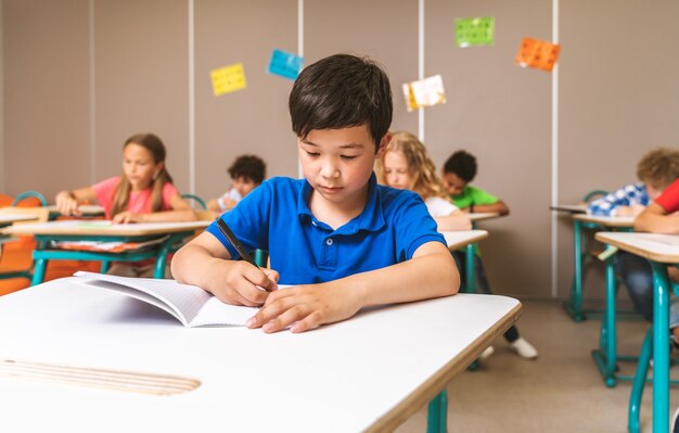 Grupo multirracial de niños en la escuela primaria: niños juguetones que disfrutan del tiempo escolar y la lección con el maestro y los compañeros de clase.