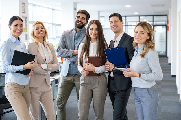 Grupo de negocios de diversidad jóvenes con ropa formal de pie en la oficina y mirando a la cámara posando y sonriendo