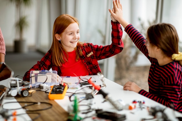 Foto grupo de niñas lindas que programan juguetes eléctricos y robots en el aula de robótica