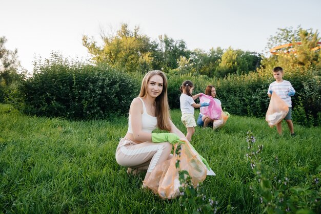 Un grupo de niñas con niños al atardecer se dedican a la recolección de basura en el parque. Cuidado del medio ambiente, reciclaje.