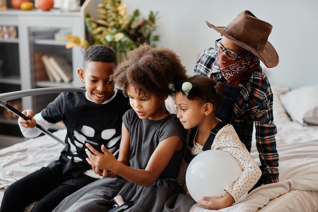 Grupo de niños afroamericanos con disfraces de halloween en casa y con smartphone