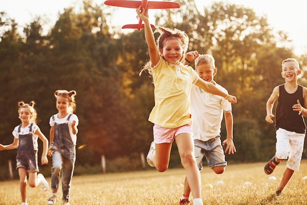 Foto grupo de niños divirtiéndose al aire libre con avión de juguete rojo en las manos.