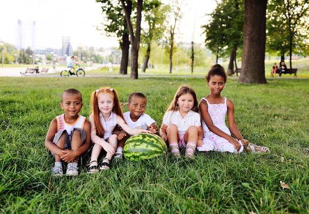 Un grupo de niños en edad preescolar en el parque sobre el césped sosteniendo una enorme sandía
