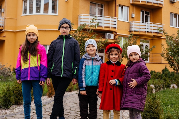 El grupo de niños de la escuela primaria se paran al fondo de un edificio de gran altura Los niños vestidos con ropa abrigada se paran al aire libre en otoño
