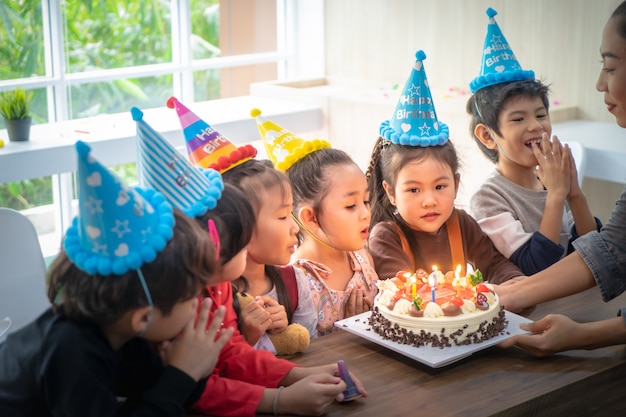 Grupo de niños está soplando pastel de cumpleaños en la fiesta de cumpleaños cantando feliz cumpleaños