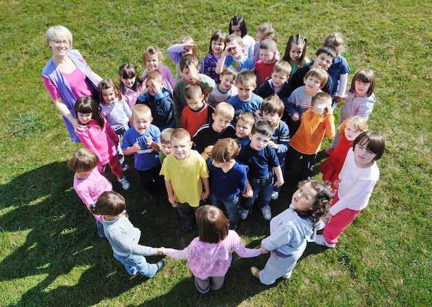 el grupo de niños felices se divierten y juegan en el concepto de educación preescolar al aire libre de jardín de infantes con el maestro