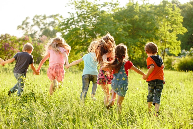 Foto un grupo de niños felices niños y niñas corriendo en el parque en el césped en un día soleado de verano.