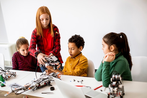 Grupo de niños felices que programan juguetes eléctricos y robots en el aula de robótica