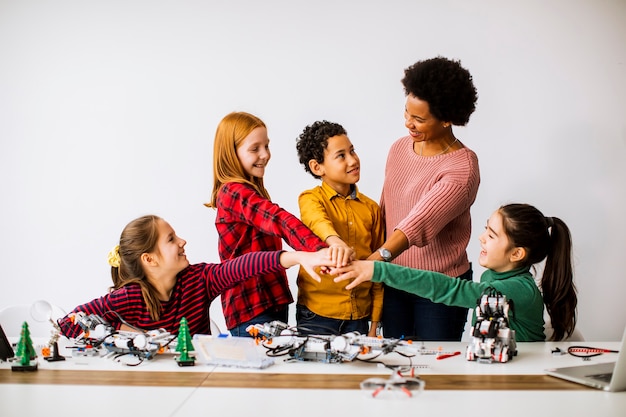 Grupo de niños felices con su profesora de ciencias afroamericana programación de juguetes eléctricos y robots en el aula de robótica